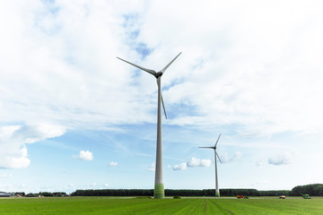 Fototapeta premium Lelystad, The Netherlands - August 31, 2018: Wind turbines standing tall in the dutch countryside generating sustainable energy for the future. You can see how the farms have become so accustom to the