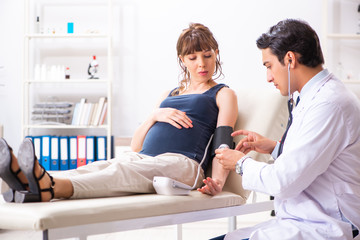 Fototapeta premium Young doctor checking pregnant woman's blood pressure