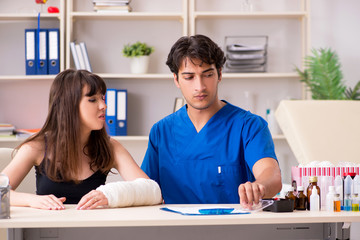 Young woman with bandaged arm visiting male doctor traumotologis