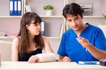 Young woman with bandaged arm visiting male doctor traumotologis