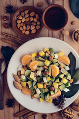 Bright vegetarian healthy avocado salad with nuts, citrus, apples and honey topping on white plate, delicious food on wooden background with set of nuts, spices, almond. Selective focus.