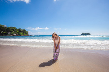 Girl wearing floral pink maxi skirt walking barefoot on the sea shore while sky is incredible blue, Thailand, Phuket