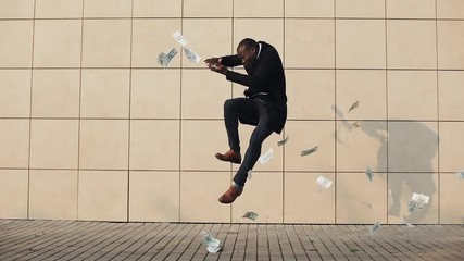 Young happy businessman scatter the dollars and funny dancing in the street. Money rain, falling dollars. It is located near the office center, slow motion. Successful business
