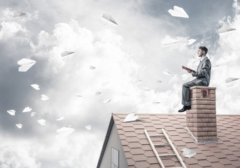 Man on brick roof reading book and paper planes flying in air