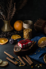 Christmas and New Year food concept. Cottage cheese pudding bake, curd pudding sweet dessert, cheesecake with black currant jam, strawberry jam, dried lemons, oranges, cinnamon on dark background.
