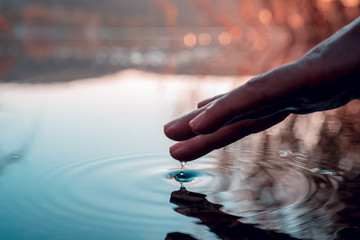 Finger touches surface of mountain lake. Hand reflection
