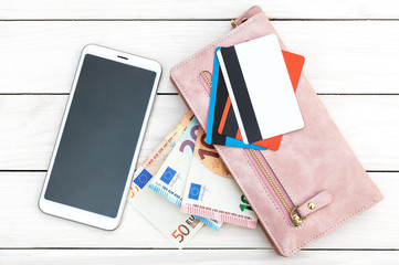 Woman's purse with credit cards and money, smartphone on white wooden background. Top view.