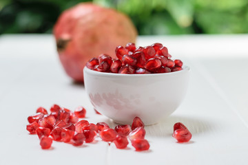 Scattered on a white table pomegranate seeds and fruits of ripe pomegranate. Vegetarian food.