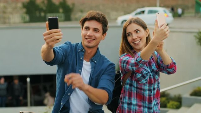 Young people are holding two smartphones and posing to the camera. Two happy young people enjoying their free time.