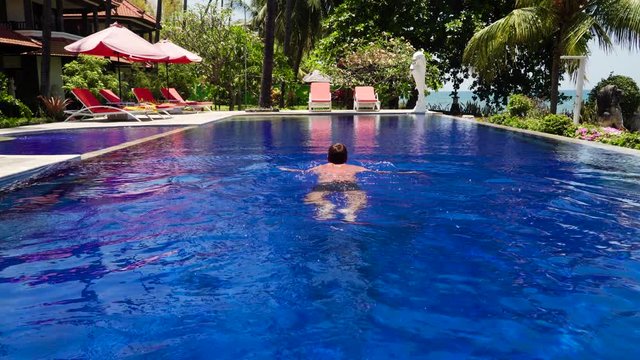 man swims in swimmingpool in luxury hotel. luxury hotel with swimming pool, sun beds, palm trees by sea. tropical resort with pool. Travel concept.