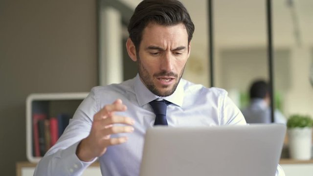 Angry businessman losing patience and screaming at laptop in modern office