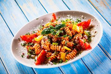 Pasta with meat, tomato sauce and vegetables on wooden table