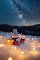 Happy snowman with gift boxes standing in winter christmas landscape. Snowman in mountains. Space landscape with silhouette mountains. Milky Way at mountains