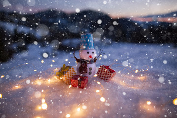 Happy snowman with gift boxes standing in winter christmas landscape. Snowman in mountains