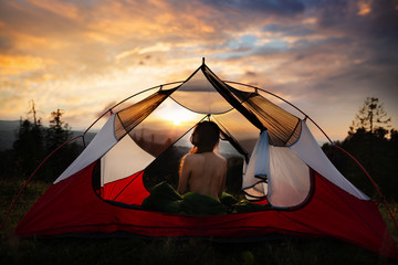 Naked woman sitting in tent in sleeping bag and enjoy the scenery in the mountains. Incredible...