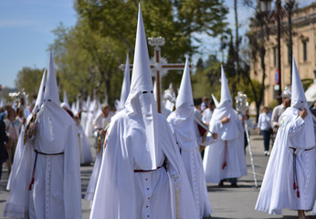 a large Catholic procession with penitents dressed in white and with a hood