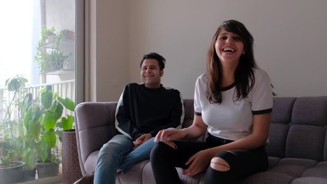 Serious young attractive couple breaks into an impromptu celebrating and laughter fit looking towards the camera