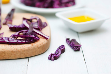 red cabbage salad ingredients with unpeeled sesame seeds and olive oil on white wood table