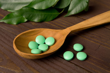 Herbal pills on wooden spoon on the background of medicinal leaves . Herbal medicine making pills