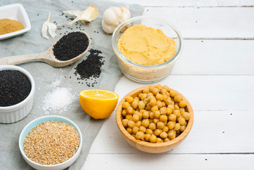 hummus spread and ingredients: chick pea, sesame seeds, garlic on creased canvas, white wood background