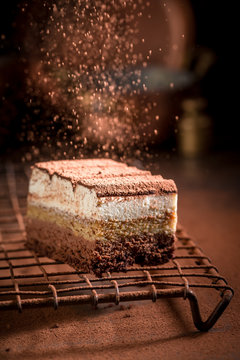 Falling Cocoa Powder On Tiramisu Cake On Metal Cooling Grid