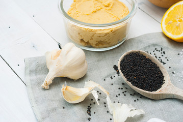 hummus spread and ingredients: chick pea, sesame seeds, garlic on creased canvas, white wood background