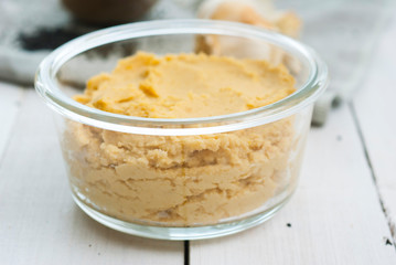 hummus spread and ingredients: chick pea, sesame seeds, garlic on creased canvas, white wood background