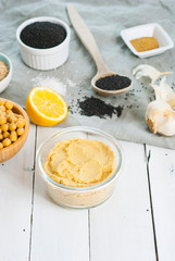 hummus spread and ingredients: chick pea, sesame seeds, garlic on creased canvas, white wood background