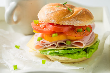 Crisp sandwich with fresh ingredients and tea on white table