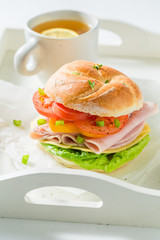 Sandwich with tomatoes, cheesem, ham and tea on white table
