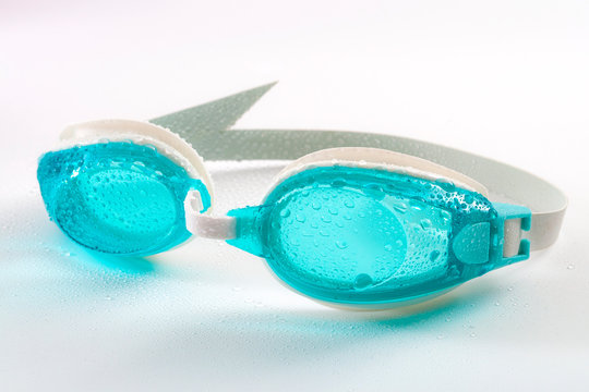 Swimming pool goggles and athletic equipment concept theme with close up on a pair of blue wet googles covered in water droplets isolated on white background