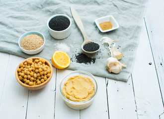 hummus spread and ingredients: chick pea, sesame seeds, garlic on creased canvas, white wood background