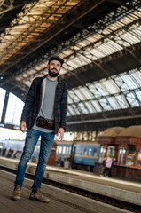 stylish bearded hipster tourist with backpack behind his shoulder on the platform of the railway station with a metal vault