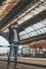 stylish bearded hipster tourist with backpack behind his shoulder on the platform of the railway station with a metal vault