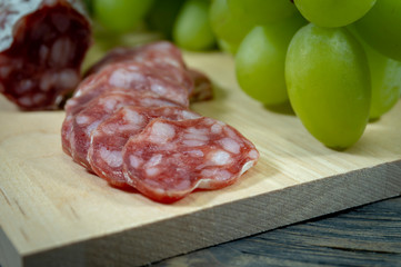 Sliced salami and grapes on wooden cutting board