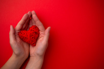 Hands hold red heart on red background