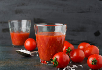 Two glasses of fresh tomatoes juice with salt, cherry tomatoes on dark background