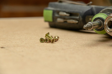 The hand drill and several screws are on the table of the joiner. The workplace of the joiner.
