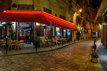 Cozy street with tables of cafe in Paris at night, France