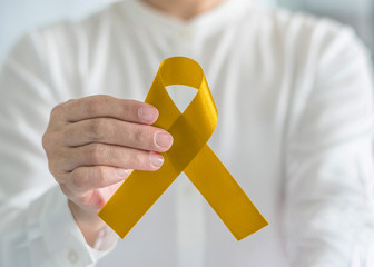 Childhood cancer awareness with Gold ribbon bow color in person's hand