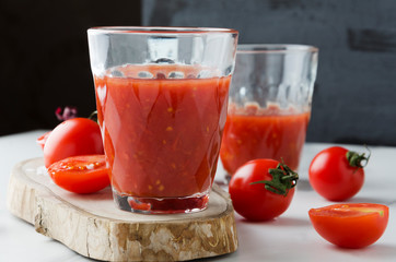 Closeup of glass of fresh pressed tomato juice on table in the kitchen.Tomatos,wooden board,glasses of tomato juice