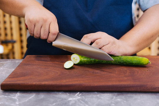 Super sharp Japanese kitchen knife cut zucchini into ultra thin slice on wooden chopping board.