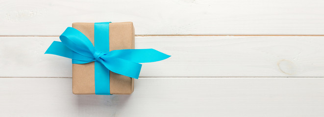 Beautiful gift box with a blue bow on the white wooden table. Top view banner with copy space for...
