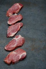 Row of fresh pieces of pork meat on grey table in the kitchen