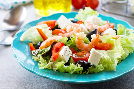 The concept of healthy and dietary food. Healthy salad close-up, Greek salad with shrimps and vegetables on a light stone or slate table.