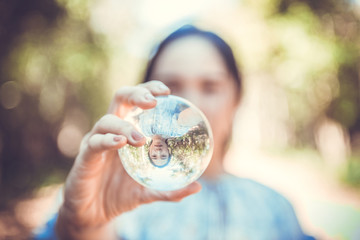 Beautiful woman hold crystal ball and can see a nice view that reflects through the big marble ball. Filtered image.