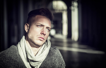 One handsome young man in urban setting in European city, standing under old, elegant colonnade