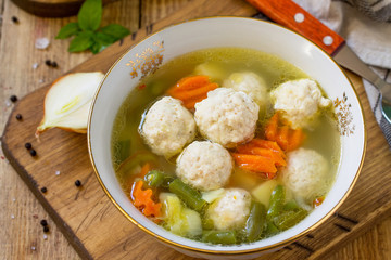 The concept Diet menu. Healthy soup with vegetables and chicken meatballs in a bowl on wooden table in rustic style. Soup close-up.