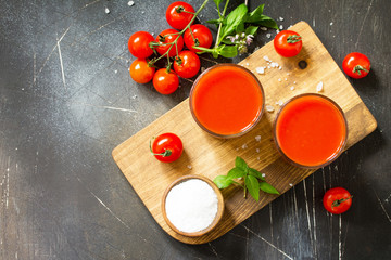 Diet nutrition concept. Glasses with tomato juice and fresh tomatoes on a dark stone table. Top view flat lay background. Copy space.