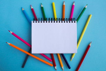 Top view of an open notepad and color pencils on the blue background.Copy space.